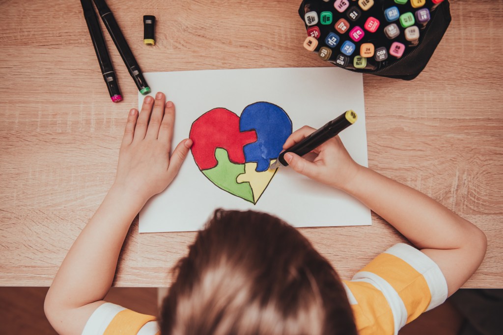 For World Autism Awareness Day, a child draws a heart from multi-colored puzzles.